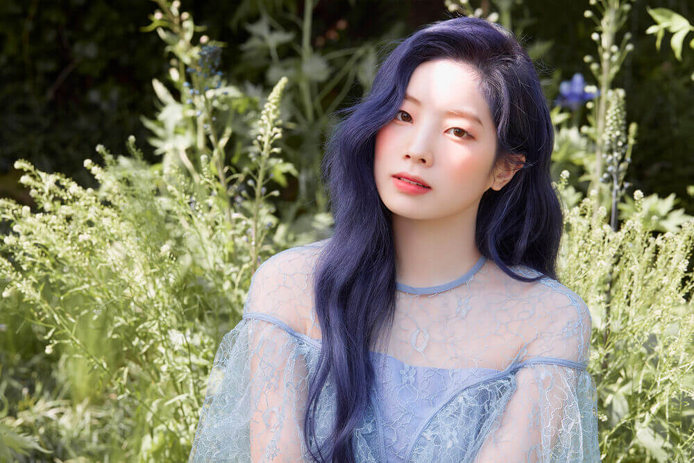 Dahyun con el cabello azul, detras de ella se encuentra mucha naturaleza