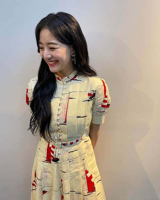 Jihyo soriendo hacia el lado con un vestido blanco con detalles en rojo